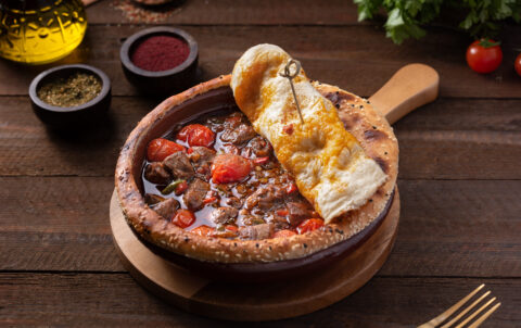 Authentic Turkish kebab with eggplant puree, yogurt, and grilled pepper served with bulgur pilaf and pickles on rustic wooden table