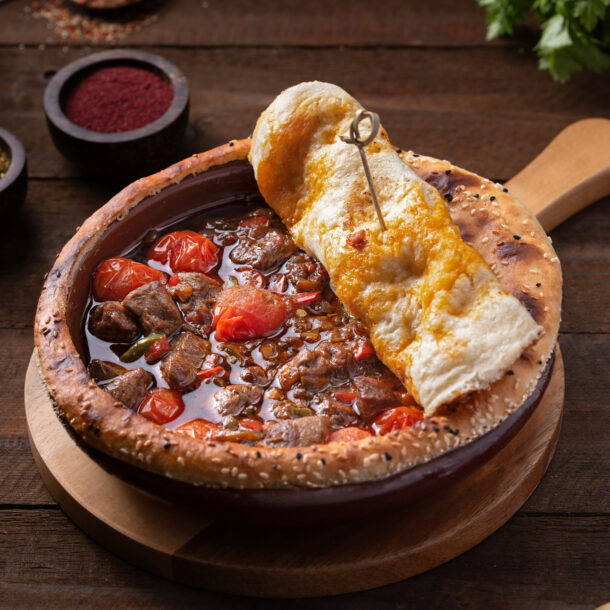 Authentic Turkish kebab with eggplant puree, yogurt, and grilled pepper served with bulgur pilaf and pickles on rustic wooden table