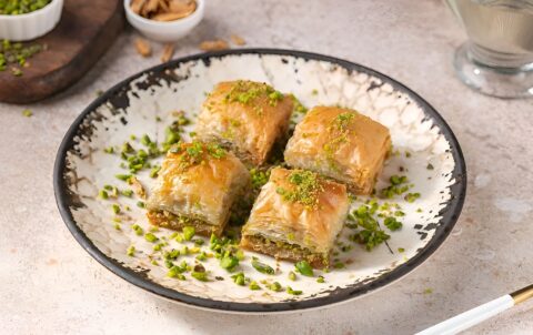 Plate of pistachio baklava pieces served with nuts and syrup.