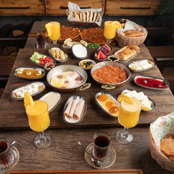 Family-style Turkish breakfast spread at a Turkish restaurant in Abu Dhabi, featuring freshly baked pide, eggs, cheeses, olives, pastries, grilled dishes, tea, and fresh juice served on a wooden table in a warm dining setting.