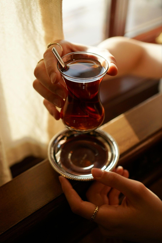 Woman’s hands holding a glass of Turkish tea on a saucer in warm sunlight, creating an elegant and cozy scene
